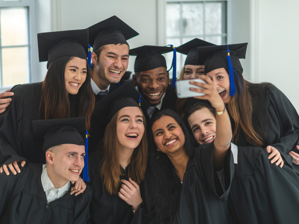 Group of diverse high school graduates in caps and gowns taking a selfie indoors