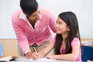 Teacher helping elementary school child with written project in classroom