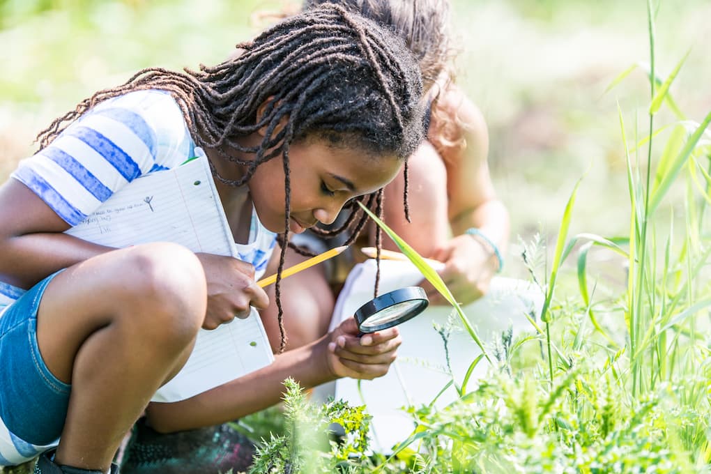 Student using magnifying glass to explore plants during outdoor science activity